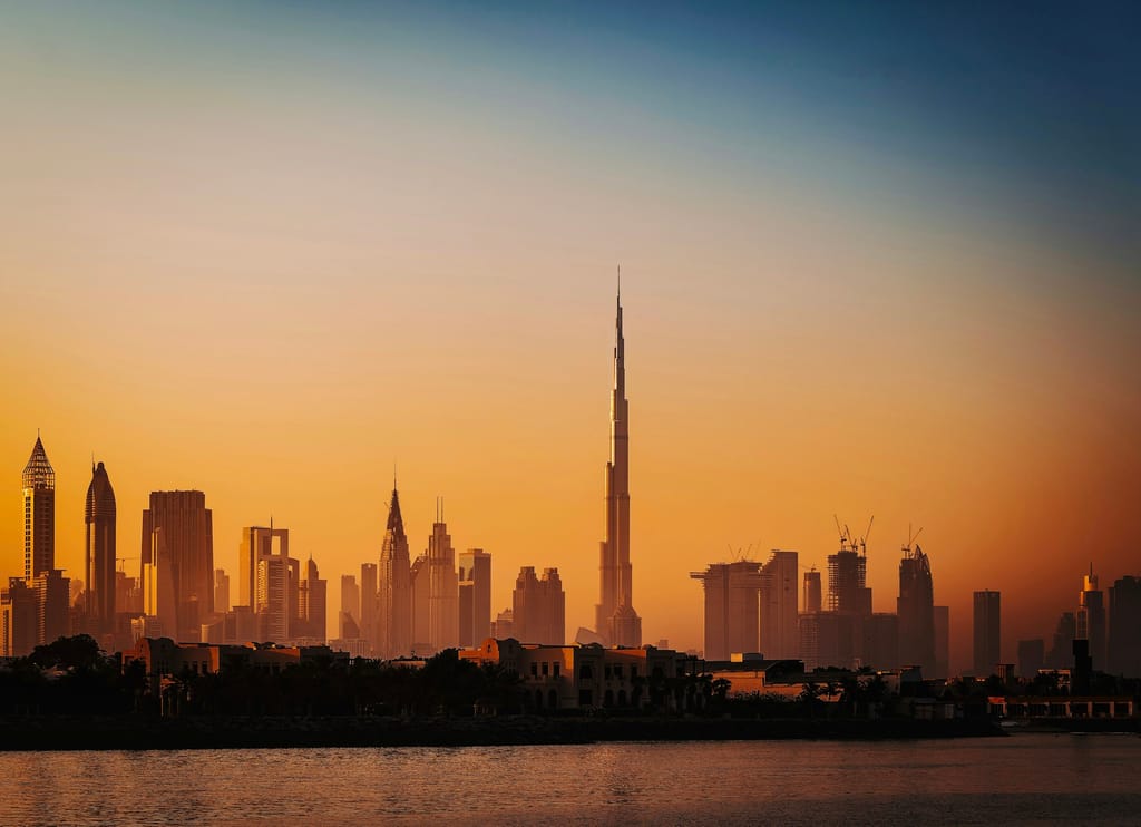 Downtown Dubai skyline and Burj Khalifa silhouetted against an amber dusk sky over water.