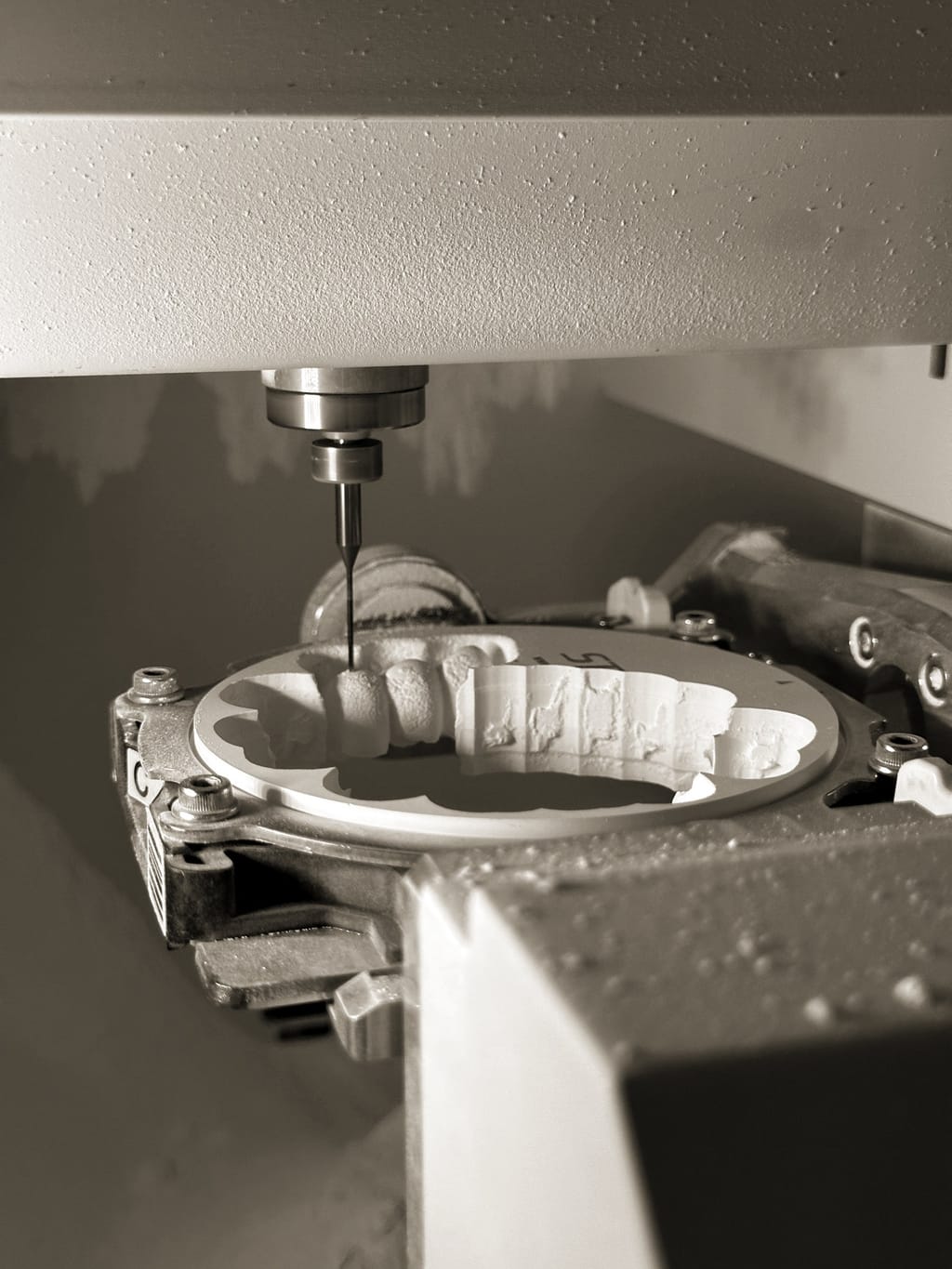 Milling bur over a white zirconia disc with several milled restorations, purple-pink machine light. (colour-graded copy: desaturated and warmed to match the site palette)